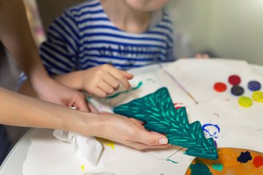 Anne ve çocuk birlikte yeni yılı tahta, doğal köknar ağacı oyuncağını yeşil renge boyuyorlar. Mutlu çocuk el yapımı Xmas sanat dekorasyonu konsepti yapıyor. Çocuklar evde hobi olarak ölüyorlar.