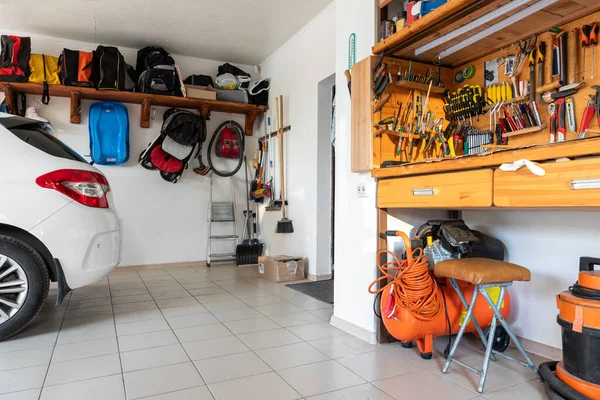Home suburban car garage interior with wooden shelf, tools equipment stuff storage warehouse on white wall indoor. Vehicle parked at house parking background. DIY workbench for repair home appliances.