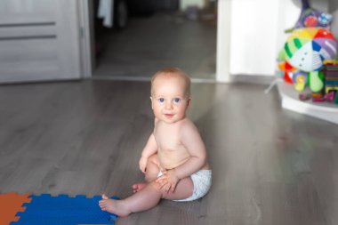 Şirin, sevimli, beyaz, küçük bebek bebek güneşli bir günde oyuncaklar ve yumuşak paspaslarla odada oynamaktan zevk alıyor. Evin içinde sürünen komik küçük çocuk. Yeni doğan büyüme ve sağlık hizmetleri.