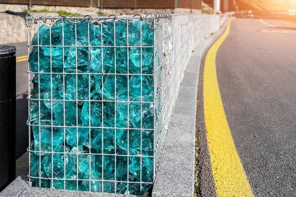 新的现代化漂亮的加布里安围栏的特写，金属笼充满碎石和破碎的人造蓝色玻璃岩石靠近沥青路面。城市街道路面保护 — 图库照片