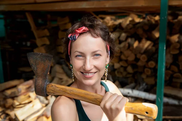 Young adult beautiful happy attractive caucasian brunette woman portrait have fun enjoy holding old rusty axe chopping firewood at wood store on backyard. Female person vintage retro pinup style