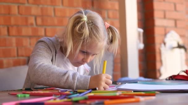 Bonito adorável caucasiano menina pequena criança loira desfrutar de pintura com lápis de cor coloridos e caderno de esboços de papel na mesa de quintal contra parede de tijolo. Crianças passatempo criativo. Criança aprendendo pintura no estúdio de arte — Vídeo de Stock