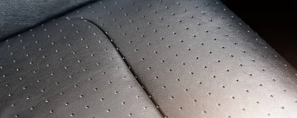 Close-up detail view of modern black perforated ventilated luxury car seat. Part of dark vehicle interior. Auto detailing and leather polish skin cleaning wash and care concept. wide banner panoramic