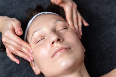 Güzellik uzmanının eli, yüz masajı için kırışıklık önleyici krem yapıyor. Güzellik kliniğindeki çekici kadın müşteriye losyon sürüyor. Kozmetik uzmanı cilt bakımı yapar. Sağlık terapisi.