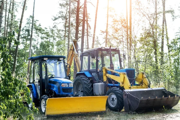 Dos pequeños y grandes tractores modernos estacionados en el patio trasero cerca de la granja forestal en el campo. Equipamiento técnico y agrícola residencial. Maquinaria aparcada para mantenimiento y almacenamiento al aire libre — Foto de Stock