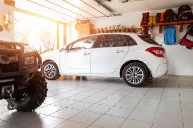Ev banliyösü modern araba ve ATV çift katlı garaj içi ahşap raf, aletler ve malzeme depolama deposu güneş ışığına karşı kapalı. Park halindeki aracın arka planı.