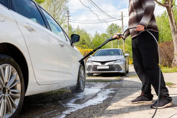 Закрытая деталь автомойка с водяным насосом высокого давления на заднем дворе дома в яркий светлый летний день. Автомобиль покрыт пенным шампунем химическими моющими средствами во время автомойки самообслуживания — стоковое фото