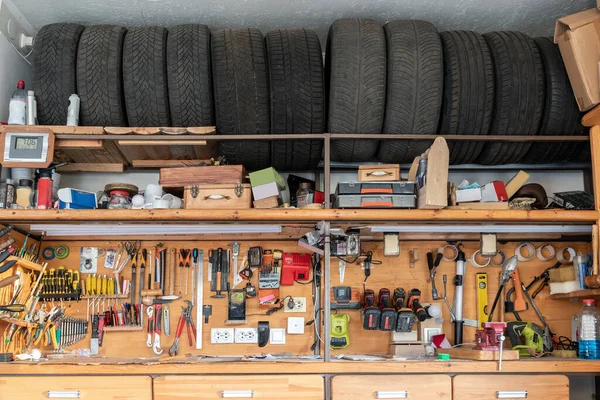 Home suburban garage interior big wooden workbench with lot of power mechanic tools at background. Spare season wheels storage shelf rack ceiling warehouse. DIY, self service and repair