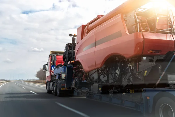 Zware industriële vrachtwagen met oplegger platform transport gedemonteerd combineren oogstmachine op de openbare weg op zonsondergang zonsopgang dag. Vervoer van landbouwmachines — Stockfoto