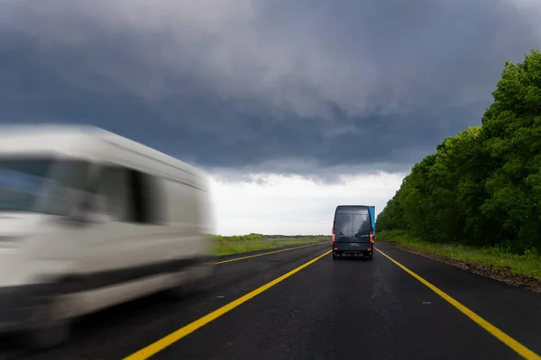 Бак доставки небольшого грузового грузового фургона курьерской доставки быстро движется по мокрой дороге в городской пригород под дождливым облачным небом. Бизнес-дистрибуция и логистический экспресс-сервис. Мини-автобус — стоковое фото