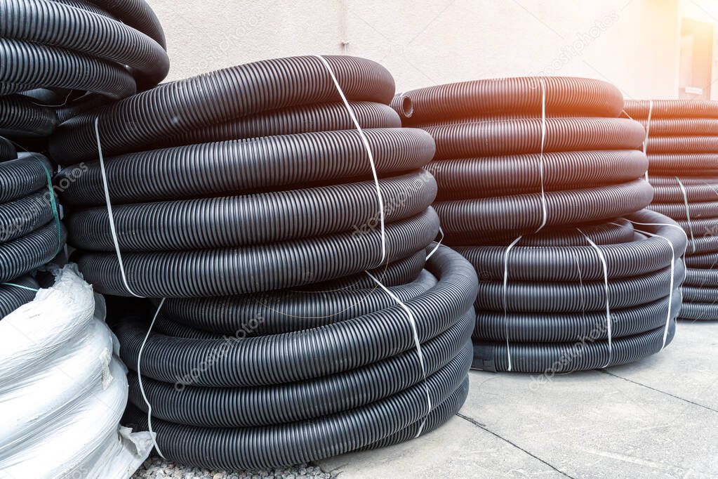 Many rolled colis of new black corrugated goffred plastic electric plumbing drainage pipe prepared for installation near building construction site. Drain sewage tube hose conduit pipeline