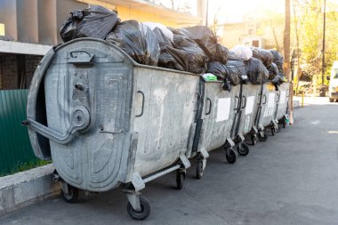 Şehir merkezindeki ya da banliyödeki konut binasının yakınındaki siyah plastik çöp torbalarıyla dolu büyük metal çöp bidonları. Geri dönüşümsüz çöp toplama