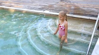 Küçük sevimli, sevimli sarışın, oyuncu, beyaz, aktif okul kızı yazın açık deniz tatil köyünde havuz kenarında yüzmeyi seviyor. Mutlu çocuk arkadaş tatil gezisi konsepti