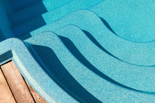 Новий сучасний пластиковий басейн зі скловолокна вхідний крок з чистою свіжою освіжаючою блакитною водою в яскравий спекотний літній день на подвір'ї або курортному готельному спа-центрі. Дерев'яна підлогова палуба з тикового або модрини — стокове фото