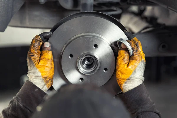 Closeup male tehnician mechanic greasy hands in gloves install new car oem brake steel rotor disk during service at automotive workshop auto center. Vehicle safety checkup and maintenance concpet — Stock Fotó