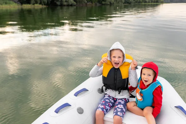 Twee schattige kleine Kaukasische broer en zus jongen en meisje dragen zwemvest plezier te hebben genieten rijden opblaasbare motorboot op de rivier of het meer met familie. Kinderen zomer activiteit veiligheid recreatie — Stockfoto