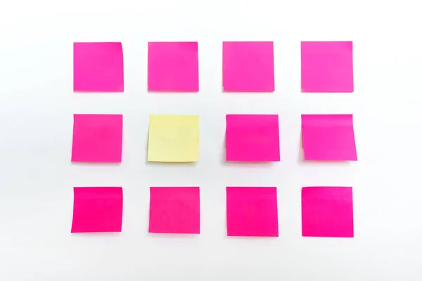 一排排五颜六色的明亮的空粉色粘贴纸和一摊黄色的贴贴在白色墙体的背景上。附上空白备忘模型做记事本 — 图库照片