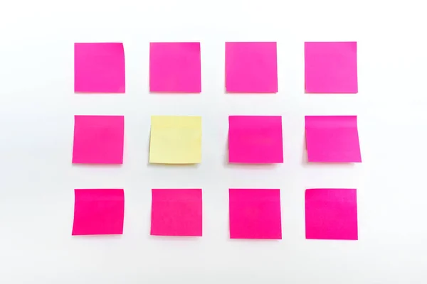 Des rangées de nombreuses notes de papier collant rose vif et vide coloré et un stand d'un autocollant jaune de type stand isolé sur fond texturé mur blanc. Modèle de mémo vierge joint pour faire le bloc-notes — Photo