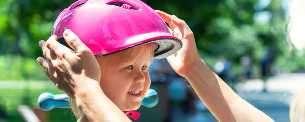 在夏天的日子里，妈妈在户外骑自行车或摩托车的时候，给可爱的金发碧眼的高加索蹒跚学步的小女孩戴上安全帽。儿童体育活动保护护理 — 图库照片