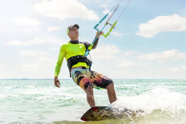 Junge erwachsene kaukasisch fitte männliche Person genießt das Reiten eines Kitesurfbretts im Sonnenschutzanzug an einem strahlend sonnigen Tag vor blauem Himmel am Meer oder an der Küste. Wassersport Adrenalin Spaß Abenteuer Aktivität — Stockfoto