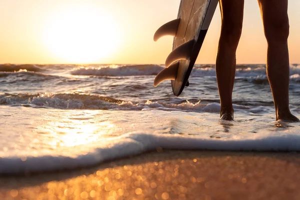 Close-up punto di vista inferiore giovane adulto surfista ragazza gambe con tavola da surf stand a onda costa dell'oceano contro l'alba calda o il sole del tramonto. Sport sano spensierato libertà stile di vita vacanza concetto — Foto Stock