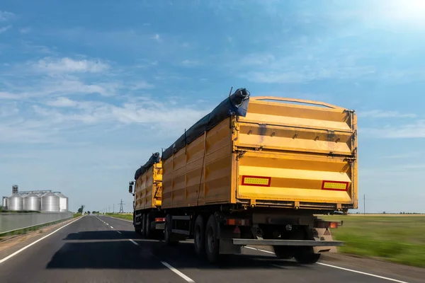 明るい夏の日に澄んだ青い空に対して荷卸しをサイロ穀物貯蔵するために高速道路を走行する大きな近代的な黄色の穀物ホッパー貨物トラック。穀物の収穫と出荷産業シーズン — ストック写真