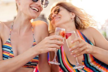 İki yetişkin kız arkadaş eğleniyor, mutlu anları kutluyor, içiyor ve okyanus kıyısı yaz tatilinde şampanya kadehlerine kadeh kaldırıyor. LGBT biseksüel yaşam tarzı ve seyahat konsepti