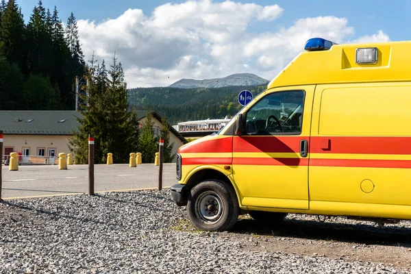 Vista laterale di giallo ambulanza soccorso ems van auto parcheggiata vicino campagna strada rurale a Highland Mountain Resort zona. Veicolo di pronto soccorso paramedico contro il paesaggio forestale alpino — Foto Stock