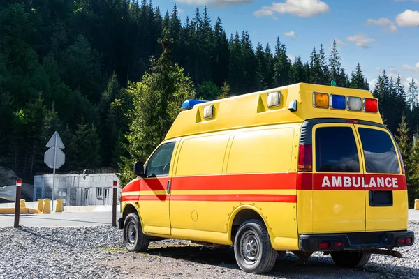 Vista laterale di giallo ambulanza soccorso ems van auto parcheggiata vicino campagna strada rurale a Highland Mountain Resort zona. Veicolo di pronto soccorso paramedico contro il paesaggio forestale alpino — Foto Stock