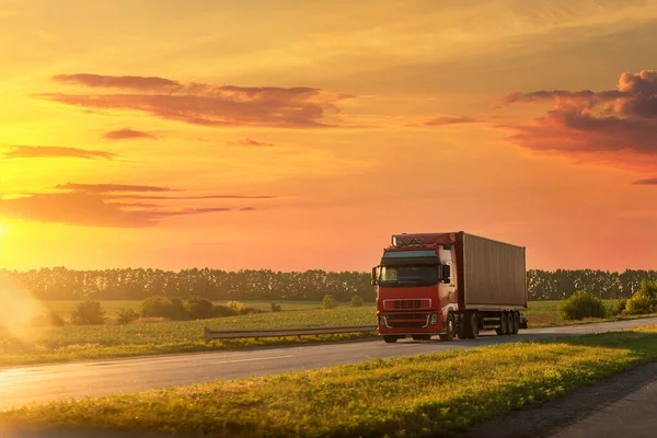 海上輸送コンテナ高速道路劇的な暖かい朝の夜の日の出の太陽の空の夕日を駆動すると風景フロントビューの大きな長い重い半小売トラック。貨物輸送業界の背景概念 — ストック写真