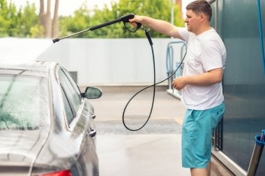 Aydınlık bir yaz gününde self-servis açık havada yüksek basınçlı su teçhizatı pompasıyla yakın plan araba yıkama. Araba oto yıkama servisi sırasında köpük şampuanla kaplı kimyasal deterjanlar.