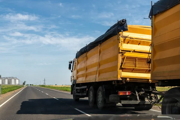 Gran camión de carga de tolva de grano amarillo moderno que conduce por carretera al almacenamiento de granero de silo que descarga el cielo azul claro aginst en el día de verano brillante. Cosecha de cereales y envío temporada industrial — Foto de Stock