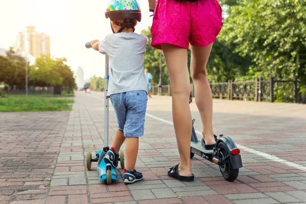 Voltar visão traseira do menino bonito com a mãe adulta jovem montando transporte de scooter no parque de rua da cidade juntos no dia ensolarado. Cuidados e apoio dos pais. Conceito de estilo de vida saudável das crianças ativas — Fotografia de Stock