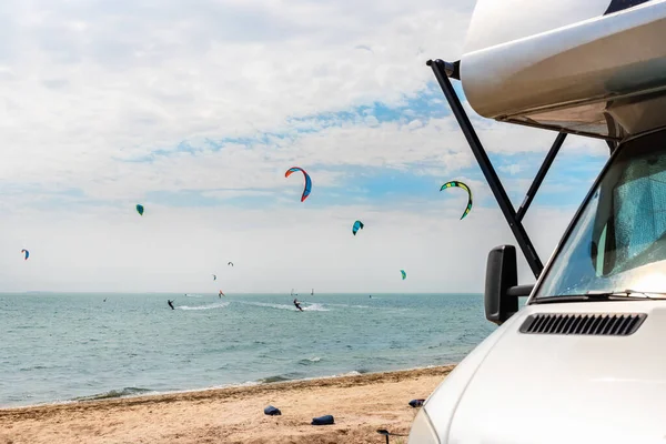Panoramautsikt över många surfbräda kite ryttare på sandstrand vattensport plats på ljusa soliga dagen mot RV husbil fordon vid havet kust surfingläger. Rolig äventyrsresa sport aktivitet — Stockfoto