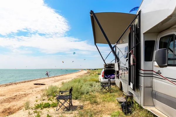 Panoramautsikt över många surfbräda kite ryttare på sandstrand vattensport plats på ljusa soliga dagen mot RV husbil fordon vid havet kust surfingläger. Rolig äventyrsresa sport aktivitet — Stockfoto