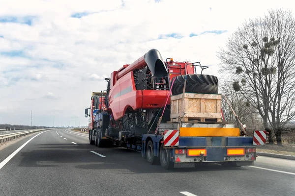 Camión industrial pesado con semirremolque plataforma de transporte desmontado cosechadora cosechadora cosechadora en carretera pública común en la puesta del sol día del amanecer. Servicio de transporte de equipos agrícolas — Foto de Stock