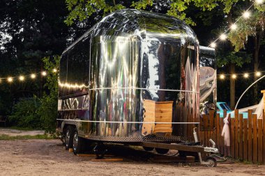 Kırsal kesimdeki ahşap çitlerin yakınına park edilmiş gelecekten kalma gümüş renkli karavan karavanı manzarası ya da çelenk ağacına karşı bir çiftlik. Retro tarzı yemek kamyonu karavan aracı