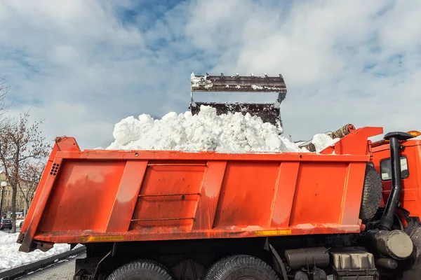 A traktorrakodó gép piszkos havat tölt fel a szemétszállító kocsira. A város utcájának megtisztítása, a hó és a jég eltávolítása nehéz hóesések és hóvihar után. Hóeke szabadban tiszta járda járda út felhajtó — Stock Fotó