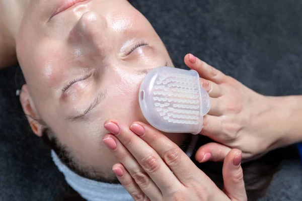 Közelkép kozmetikus orvos kézimunka anti-age eljárás arc masszázs szilikon kesztyű alkalmazása krém vonzó női ügyfél a kozmetikai klinikán. A kozmetológus bőrápoló. Egészségügyi kezelés — Stock Fotó