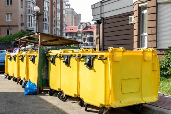 Fileiras de muitas latas grandes de plástico amarelo lixeira cheia de sacos de lixo de plástico preto lixo perto de edifício residencial no centro da cidade ou área suburbana. Coleta de lixo de triagem não reciclável — Fotografia de Stock