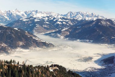 Manzaralı panoramik manzara. Kaprun Zell vadisi. Görkemli dağların arasında açık mavi gökyüzü var. Sabah sisi donmuş tarlaları sürüklüyor, sakin bir kış manzarası yaratıyor saf dağ güzelliği..