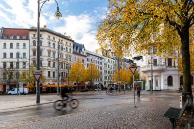 Magdeburg, Almanya - 16 Ekim 2025: Manzaralı sonbahar şehri Magdeburg Hasselbachplatz 'ın ıslak, canlı asfalt görünümünü gösteriyor. Hareket bulanıklığı dinamik kontrastlı şehir atmosferi.