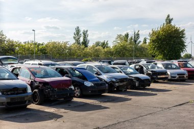 Parçalanmış arabaların sıraları açık avluda duruyor, kayıp parçaları gösteriyor, iç kısımları açıkta. Manzara hurdalık atmosferi dağınık araçları, sıcak güneş ışığını ve endüstriyel çevreyi yansıtıyor.