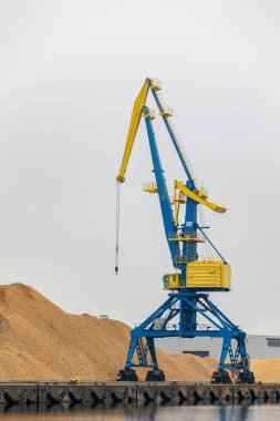 Endüstriyel liman vinç kuleleri büyük odun yığını kargo terminali solgun bulutlu gökyüzü. Deniz altyapısı sahnesinde ağır makineler ve lojistik operasyonları ithalat sanayii ithalatı vurgulanıyor.