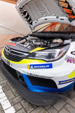 Oschersleben, Almanya - 21 Eylül 2025: Motor spor etkinliği sırasında açık kaputlu yarış arabası, motor bölmesi, aerodinamik kaporta, sponsor çıkartmaları ve pit alanının içindeki yarış lastiklerini gösteriyor.