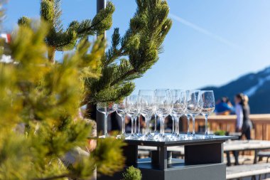 Sunlit Alp Kafe Terası 'nda boş şarap kadehleri var. Çam dalının yanındaki masada, dağ zemininde ve mavi gökyüzünde. Rahatlamış kayak atmosferi konukseverliği, seyahati, boş zamanı açık havada yakalar..