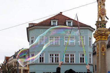 Sokak sanatçısı şehir caddesinde devasa sabun köpükleri yaratıyor, tarihi mimariye karşı gökkuşağı renkleriyle parıldıyor. Kentsel performans sahnesi yaratıcılık ve eğlence gösteriyor..