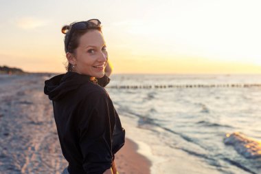Genç yetişkin bir kadının portresi, kumlu sahil kıyısında gün batımına benzeyen rüya gibi bir manzara. Sıcak bir akşam güneşi. Manzaralı refah kavramı farkındalık umudu dengeler duygusal olarak iyileşen ruh sağlığı dengesi.