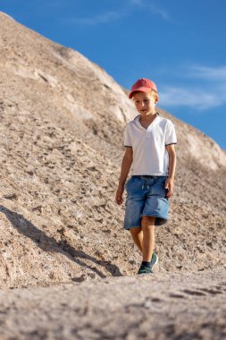 Küçük çocuk kayalık yamaçlarda yürüyor açık mavi gökyüzü bağımsızlığını gösteriyor merak sakin bir yaz macerası. Doğal taştan manzara güneş ışığı seyahat yaşam tarzı araştırmaları.