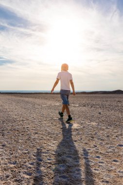 Arkaya bakan çocuk tek başına yürüyor. Ufuk çizgisine doğru kuru, kumlu bir yalnızlık. Güneş silueti özgürlüğünü ifade ediyor. Doğal taştan manzara güneş ışığı seyahat yaşam tarzı araştırmaları.